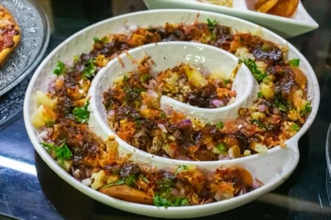 Aloo chaat served in a spiral bowl on an ornate tray.