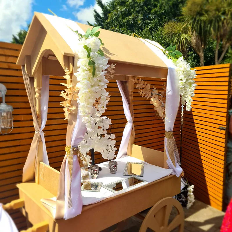 Our wooden events cart, dressed with white blossom, drapes and gold trim, set up outdoors.