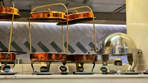A row of copper chafing dishes on gold stands.