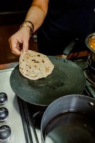 Hands laying a chapati onto a hot tava.