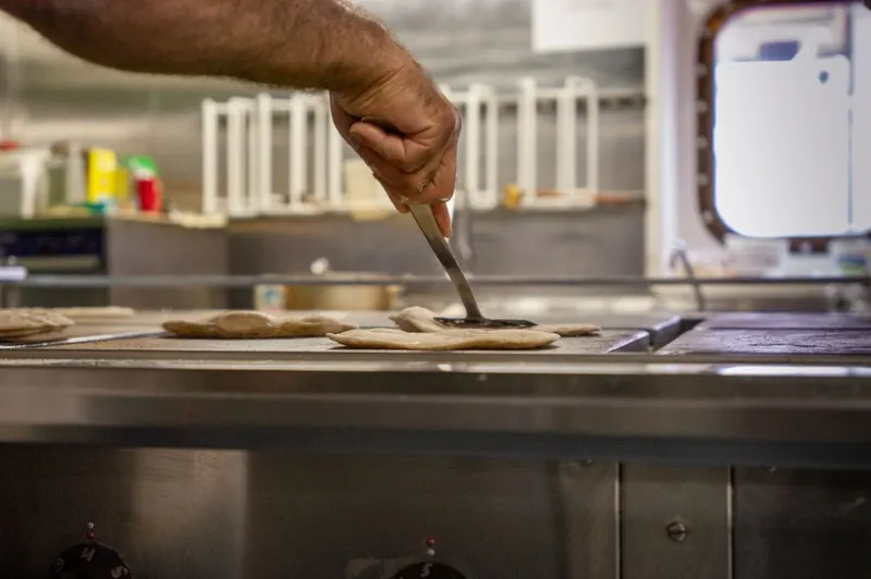 Hands pressing out flatbreads on a stainless steel worktop.