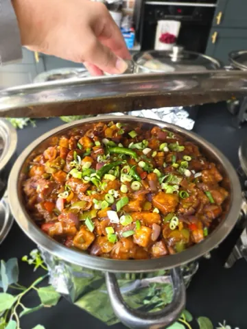 Chilli paneer in a chafing dish, finished with spring onion and green chilli.