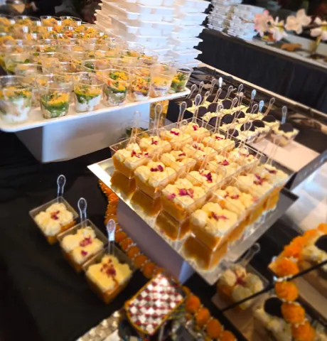 Our dessert corner: tiers of individual dessert pots and chaat glasses among marigold garlands.