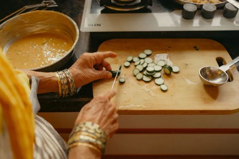 Hands with bangles slicing vegetables on a board beside a bowl of batter.