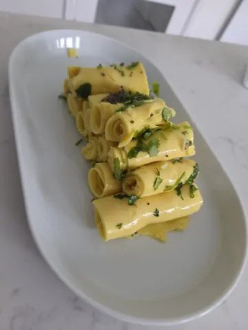 Rolled khandvi on a white plate, scattered with coriander and mustard seed.