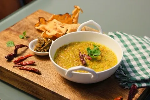 A bowl of dal with a crisp flatbread on a wooden board.