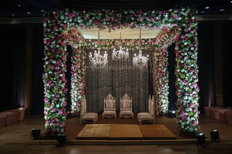 An indoor mandap dressed with a floral arch beneath chandeliers.