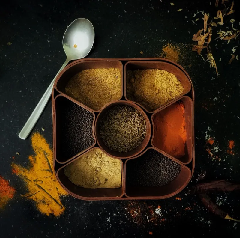 A masala dabba seen from above, its small bowls filled with different whole and ground spices.