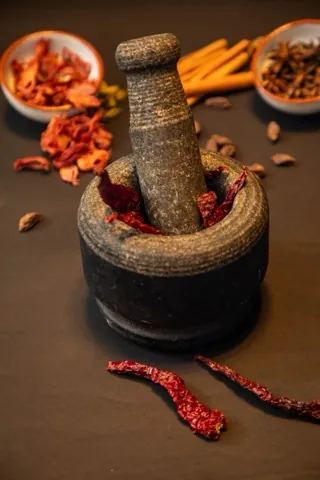 A stone mortar and pestle with dried red chillies, star anise and cinnamon.