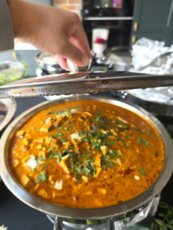 A chafing dish of paneer butter masala at one of our events, the lid lifted and the coriander just scattered.