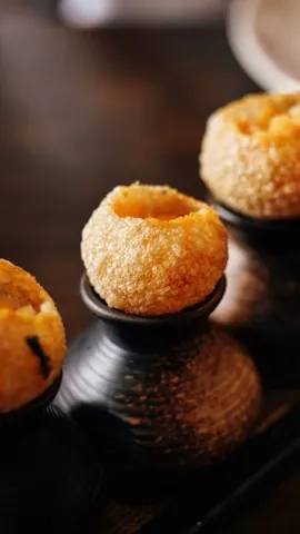 Two filled pani puri close up on dark wooden stands.