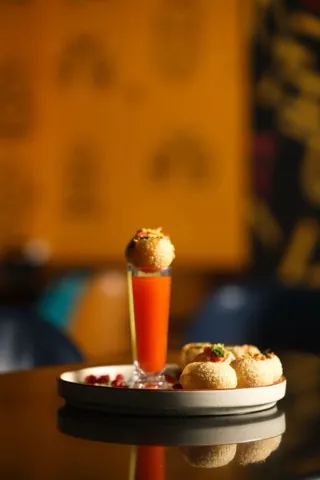 A single filled pani puri on a dark serving stand beside a shot of chutney.