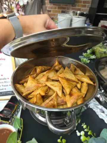 Freshly fried samosas filling a chafing dish at an event.