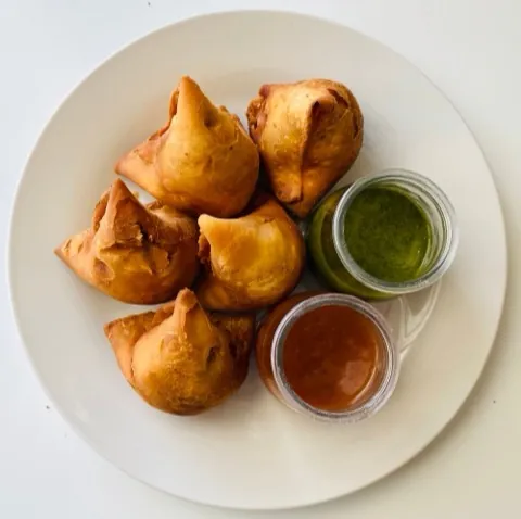 Samosas on a plate with green and tamarind chutneys.