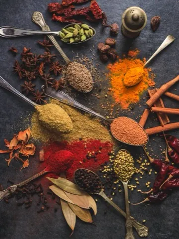 Spoons of different ground spices laid out on dark slate.
