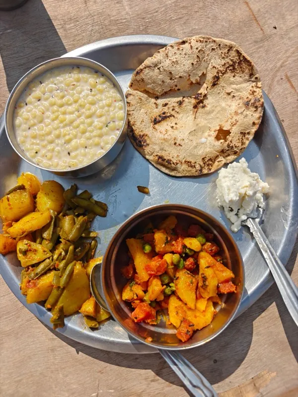 A steel thali of roti with vegetable dishes and yoghurt.