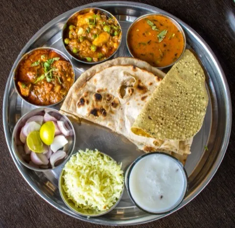 A steel thali of flatbread, vegetable dishes and raita.