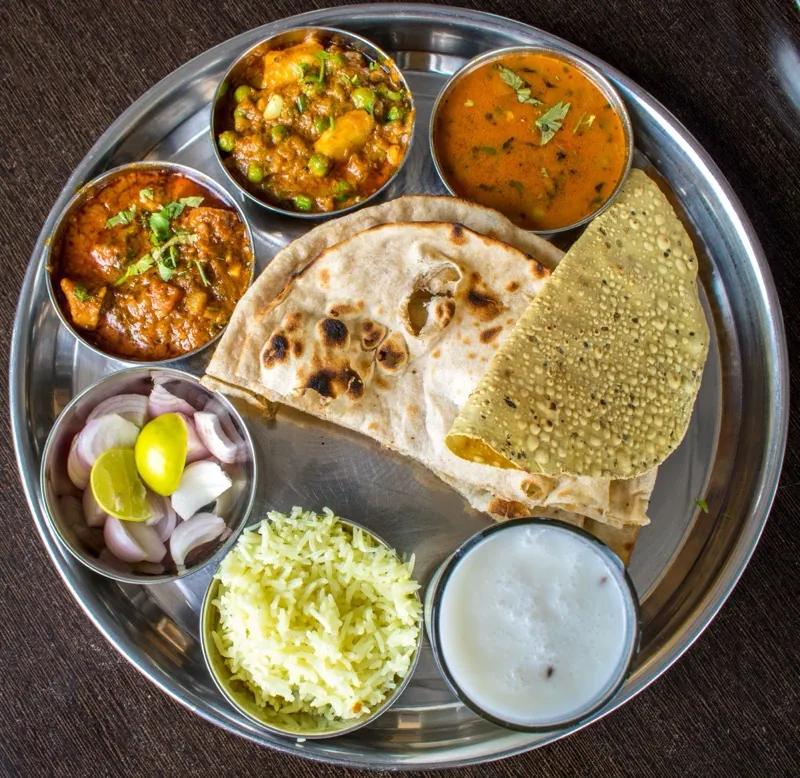 A steel thali laid with flatbread, two vegetable dishes and raita.