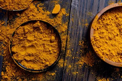 Ground turmeric in rustic wooden bowls on dark wood.