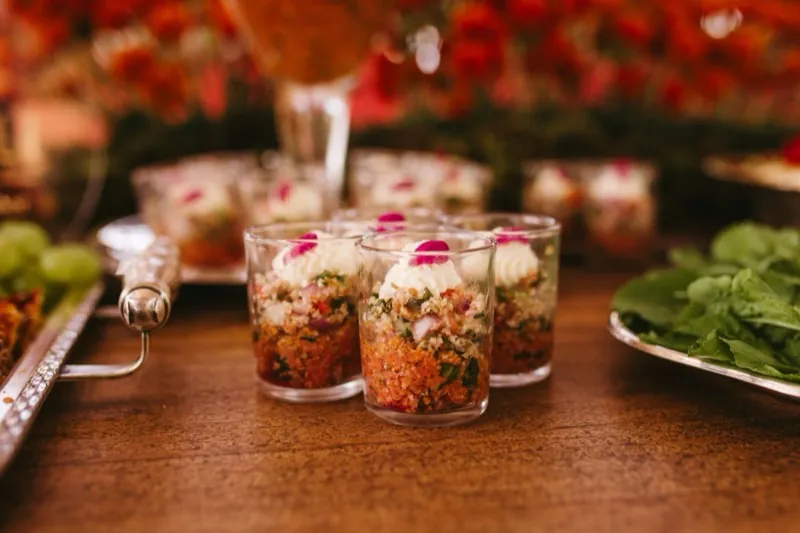 Individual chaat glasses topped with cream and rose petals, arranged on a dressed serving table.